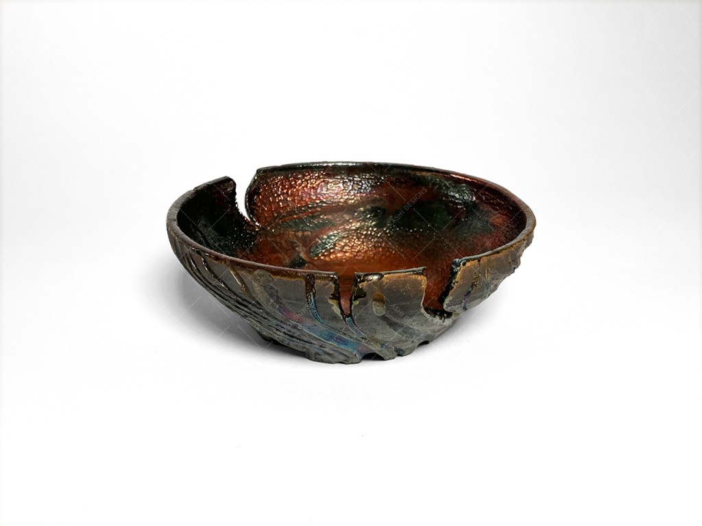 A small bowl with carved ridges and cuts like tree bark. It has a matte black finish on the outside and lustrous copper between the ridges and on the exterior.